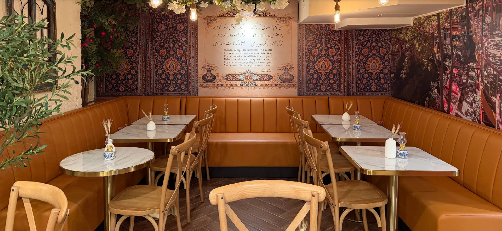 Symmetrical banquette seating with Persian tapestry and Shiraz garden mural at Taftoon NYC